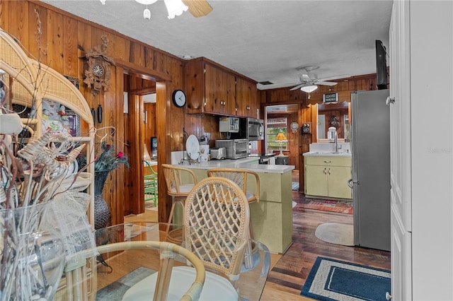 kitchen with sink, stainless steel appliances, kitchen peninsula, wood walls, and a textured ceiling