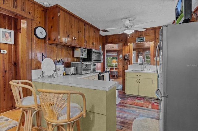 kitchen with kitchen peninsula, a textured ceiling, stainless steel appliances, ceiling fan, and sink