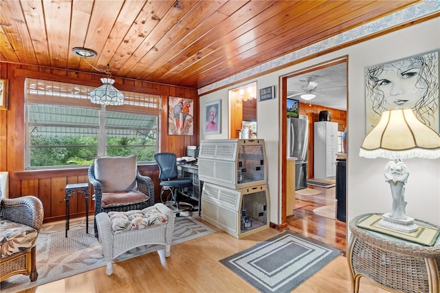 sitting room with ceiling fan, wood walls, light wood-type flooring, and wooden ceiling