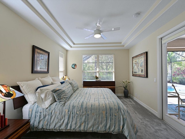 carpeted bedroom with ceiling fan, access to exterior, multiple windows, and a tray ceiling