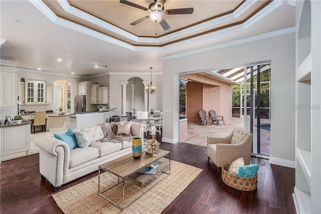 living room featuring crown molding, dark hardwood / wood-style flooring, ceiling fan with notable chandelier, and a tray ceiling