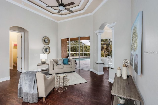 living room with a high ceiling, dark hardwood / wood-style floors, a raised ceiling, ornamental molding, and ceiling fan