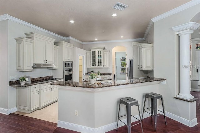 kitchen featuring kitchen peninsula, crown molding, stainless steel appliances, white cabinets, and decorative columns