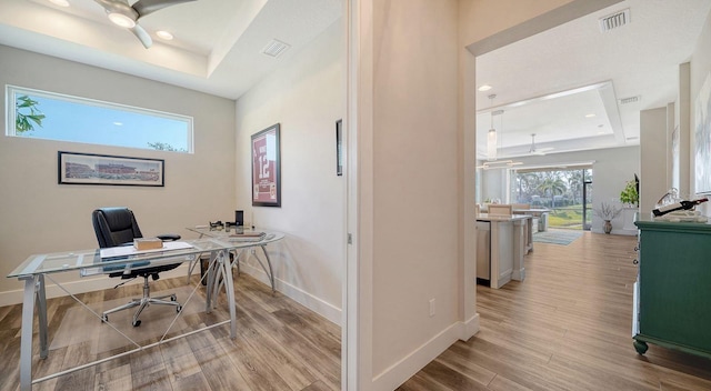 office with a raised ceiling, ceiling fan, and light hardwood / wood-style flooring