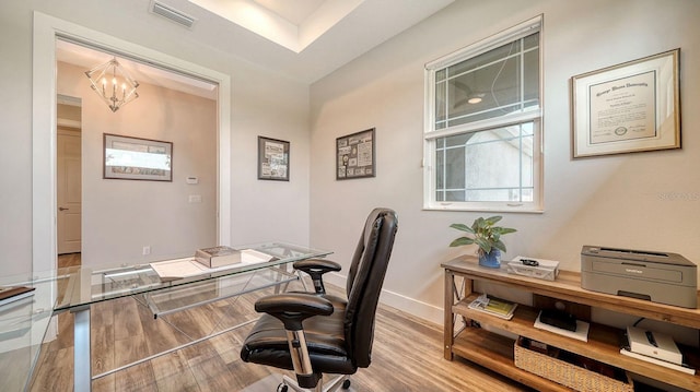 office with light hardwood / wood-style flooring and an inviting chandelier