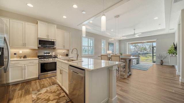 kitchen with appliances with stainless steel finishes, a raised ceiling, ceiling fan, sink, and decorative light fixtures