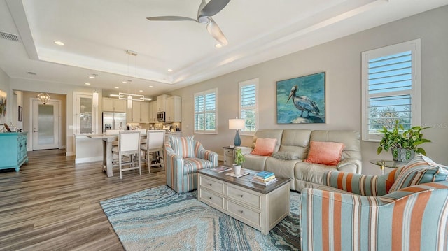 living room with ceiling fan, a raised ceiling, and light wood-type flooring