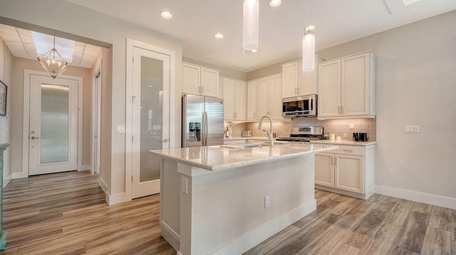 kitchen with light stone countertops, backsplash, stainless steel appliances, white cabinetry, and an island with sink