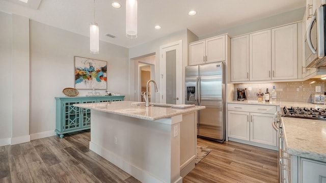 kitchen featuring light stone countertops, sink, hanging light fixtures, stainless steel appliances, and an island with sink