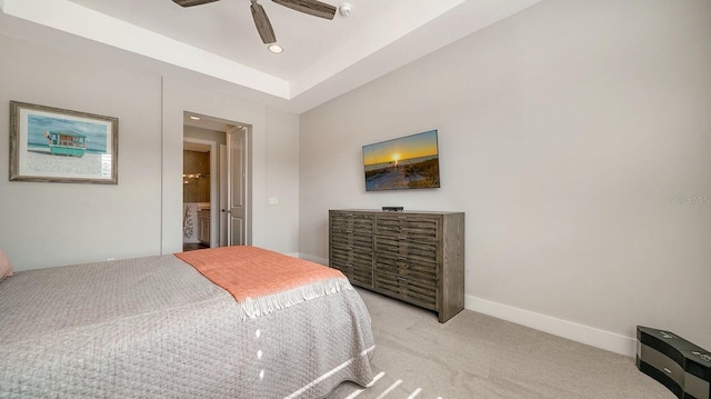 bedroom featuring ceiling fan, light colored carpet, connected bathroom, and a tray ceiling