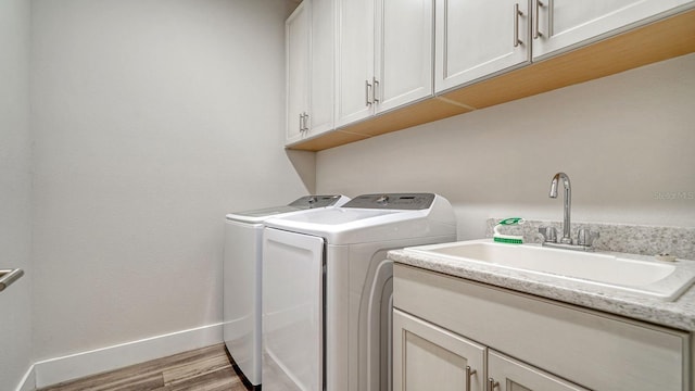 clothes washing area featuring cabinets, separate washer and dryer, sink, and light hardwood / wood-style flooring