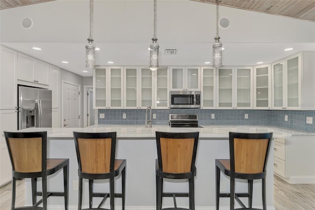 kitchen with appliances with stainless steel finishes, white cabinets, pendant lighting, light stone counters, and lofted ceiling