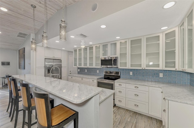 kitchen featuring decorative light fixtures, white cabinetry, light stone counters, a center island with sink, and stainless steel appliances