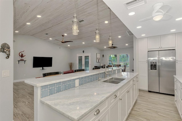 kitchen with stainless steel refrigerator with ice dispenser, sink, white cabinets, and a spacious island