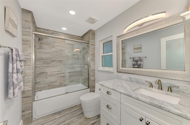 full bathroom with wood-type flooring, bath / shower combo with glass door, toilet, and vanity