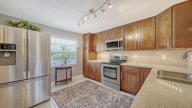 kitchen featuring light stone countertops, sink, tasteful backsplash, light tile patterned flooring, and appliances with stainless steel finishes