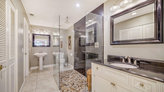 bathroom with a tile shower, toilet, and double sink