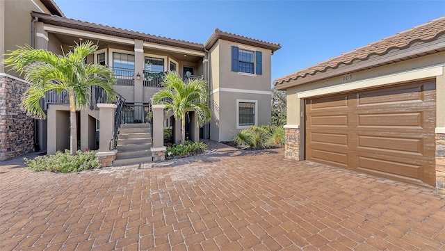 mediterranean / spanish house featuring a garage, stairway, a tiled roof, decorative driveway, and stucco siding