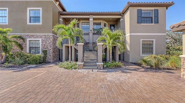 view of front of house with stone siding, a tile roof, stairway, and stucco siding