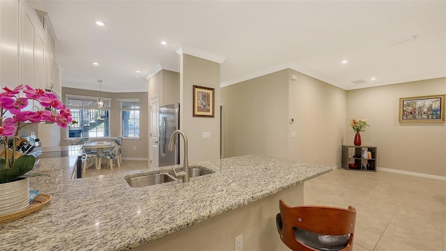 kitchen with white cabinets, light stone counters, ornamental molding, freestanding refrigerator, and a sink