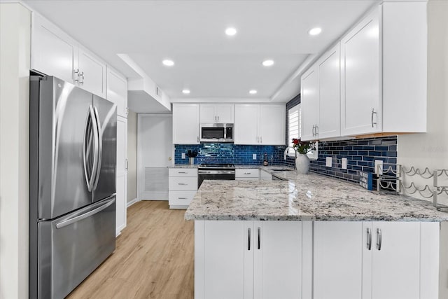 kitchen featuring white cabinetry, stainless steel appliances, sink, kitchen peninsula, and light stone counters