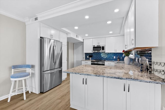 kitchen featuring kitchen peninsula, appliances with stainless steel finishes, white cabinets, and light stone counters