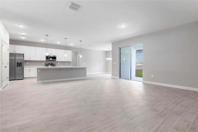 kitchen with white cabinetry, sink, stainless steel appliances, decorative light fixtures, and a center island with sink