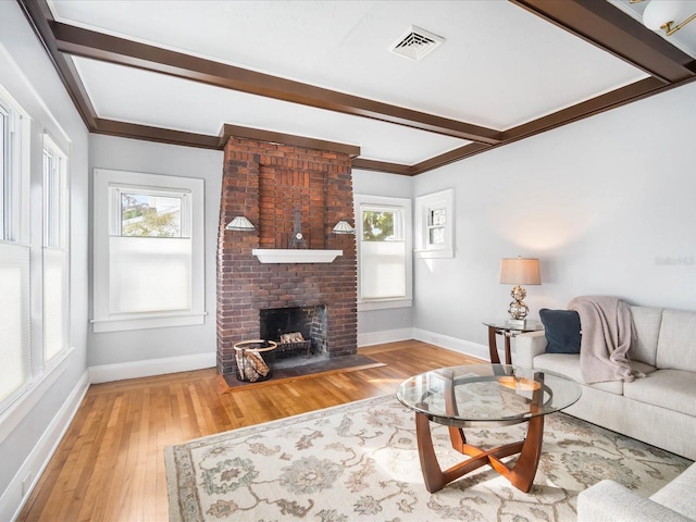 living room with beamed ceiling, light wood-type flooring, crown molding, and a brick fireplace