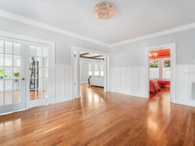 empty room featuring light hardwood / wood-style floors, ornamental molding, french doors, and a chandelier