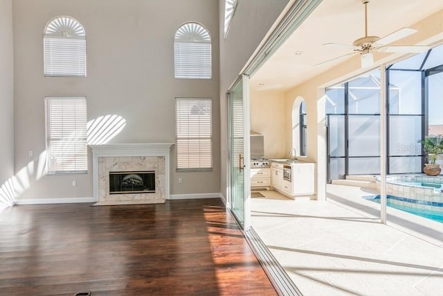 unfurnished living room with a premium fireplace, a towering ceiling, ceiling fan, and wood-type flooring