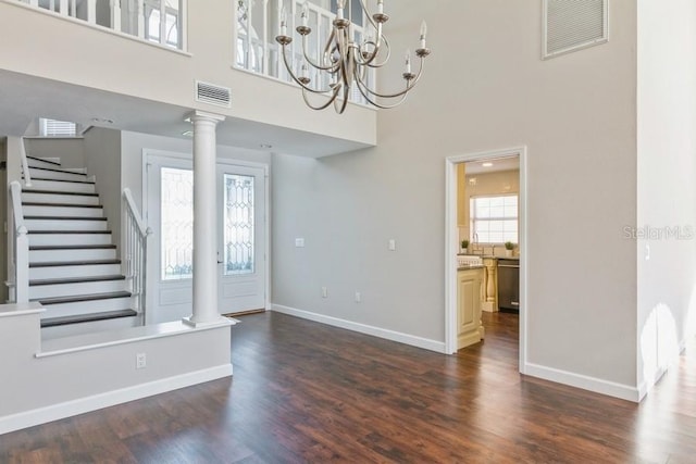 foyer featuring ornate columns, dark wood-type flooring, a towering ceiling, and an inviting chandelier