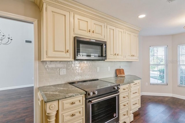 kitchen featuring appliances with stainless steel finishes, tasteful backsplash, dark wood-type flooring, cream cabinets, and dark stone countertops