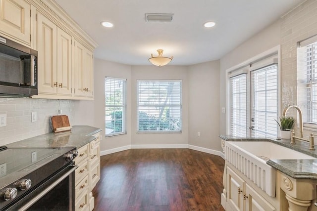 kitchen featuring cream cabinetry, electric range, a wealth of natural light, and dark stone counters