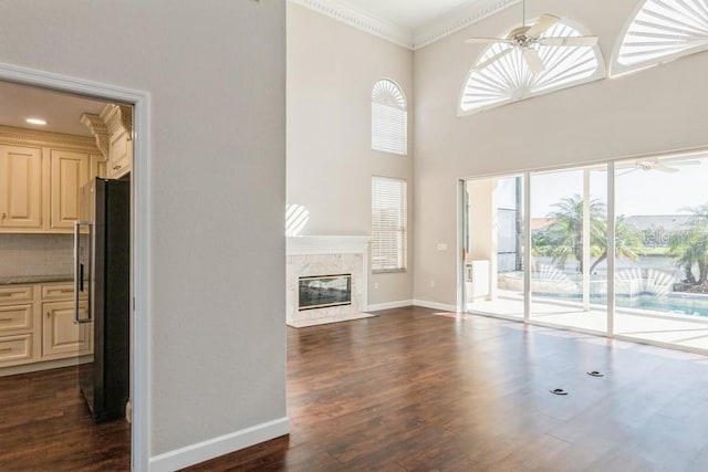 unfurnished living room with dark hardwood / wood-style flooring, a towering ceiling, crown molding, and a high end fireplace