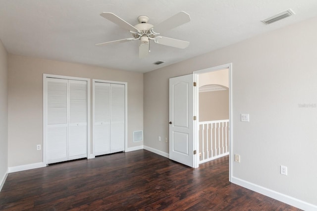 unfurnished bedroom with ceiling fan, dark wood-type flooring, and two closets