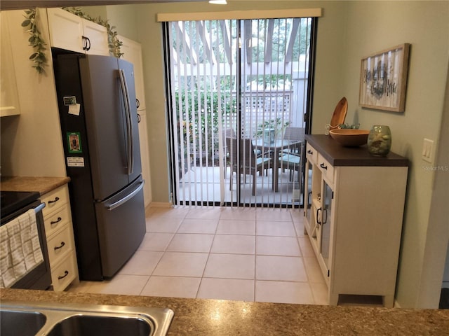 kitchen featuring stainless steel refrigerator, white cabinets, light tile patterned flooring, and black / electric stove