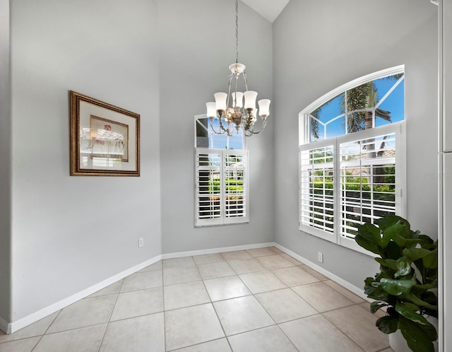 empty room featuring a towering ceiling, light tile patterned flooring, and an inviting chandelier