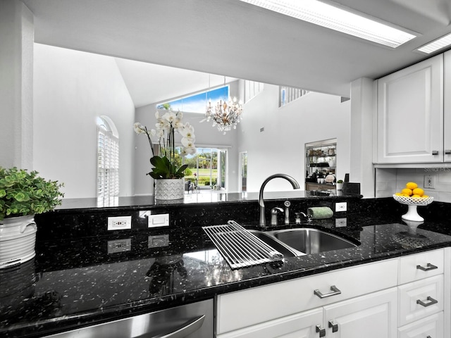 kitchen featuring white cabinetry, sink, stainless steel dishwasher, a notable chandelier, and dark stone countertops