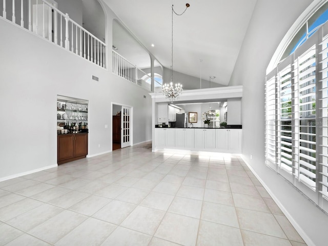 unfurnished living room with bar area, light tile patterned floors, high vaulted ceiling, and an inviting chandelier