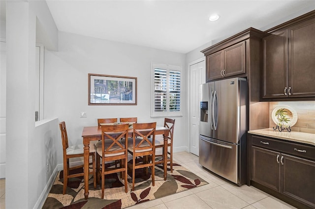 kitchen featuring decorative backsplash, stainless steel fridge, light stone counters, dark brown cabinetry, and light tile patterned floors