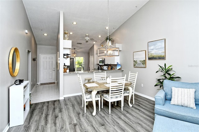 dining room with ceiling fan, wood-type flooring, and high vaulted ceiling