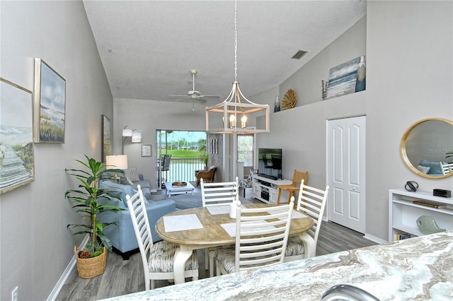 dining space with a textured ceiling, ceiling fan with notable chandelier, vaulted ceiling, and dark wood-type flooring