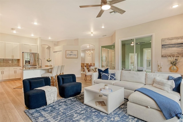 living room with light hardwood / wood-style floors and ceiling fan with notable chandelier