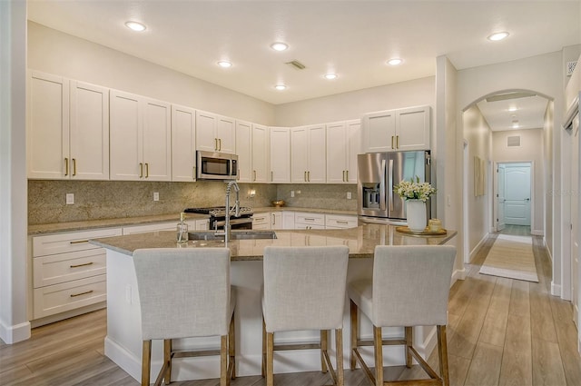 kitchen featuring light stone countertops, stainless steel appliances, a breakfast bar area, and an island with sink