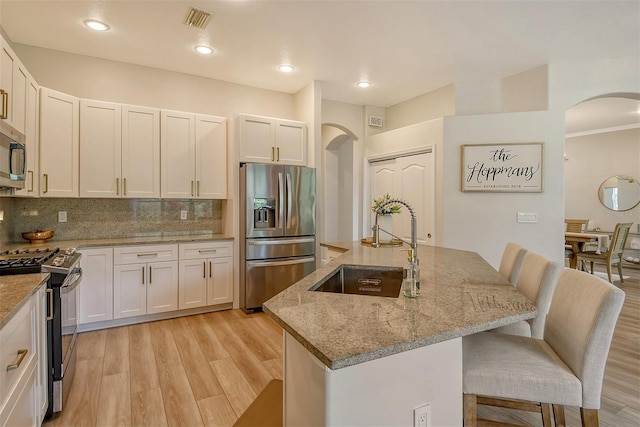 kitchen featuring light stone countertops, white cabinets, appliances with stainless steel finishes, and a kitchen island with sink