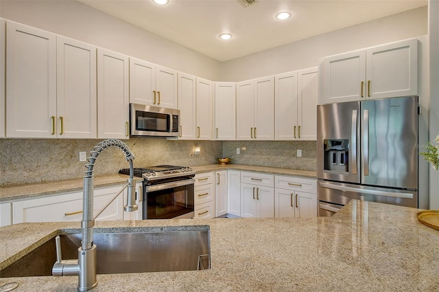 kitchen featuring white cabinetry, stainless steel appliances, decorative backsplash, light stone counters, and sink