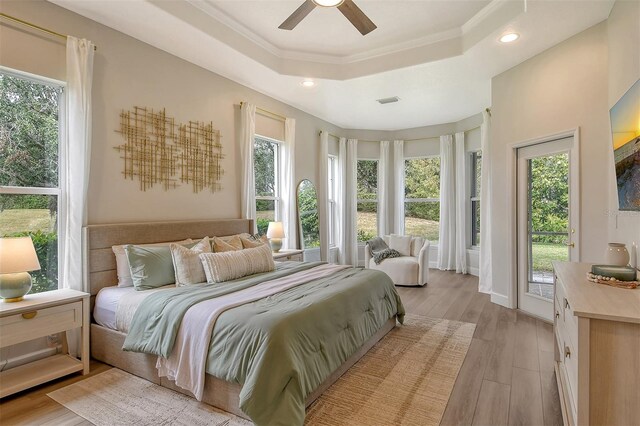 bedroom featuring ceiling fan, access to exterior, crown molding, a tray ceiling, and light hardwood / wood-style flooring