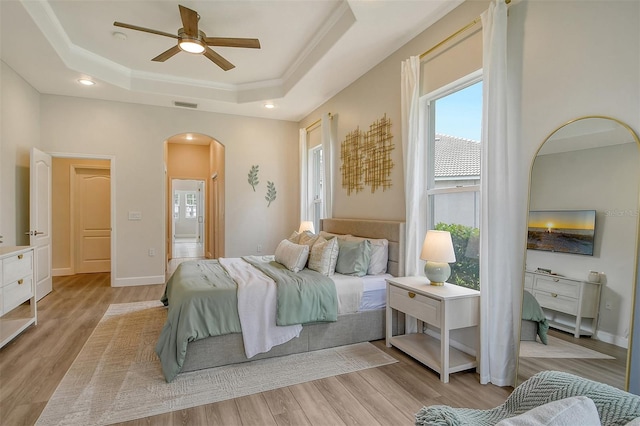 bedroom with ceiling fan, a tray ceiling, ornamental molding, and light hardwood / wood-style floors