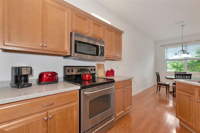 kitchen with light stone counters, hanging light fixtures, appliances with stainless steel finishes, and light hardwood / wood-style flooring