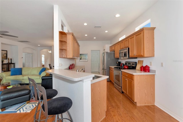 kitchen with a kitchen breakfast bar, sink, light hardwood / wood-style flooring, kitchen peninsula, and stainless steel appliances